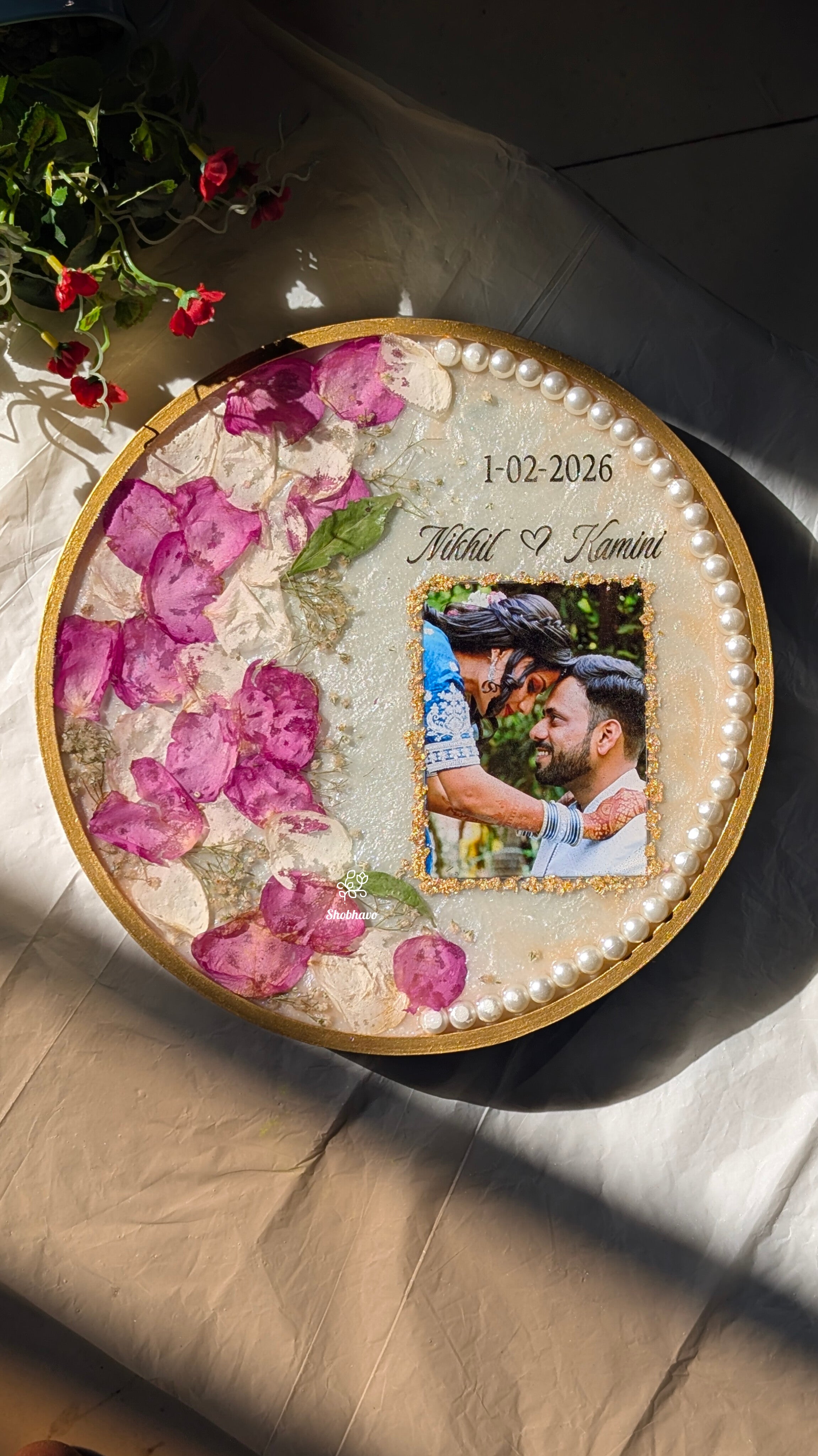 Round decorative item with pink flowers and a couple's photo, placed on a textured surface.
